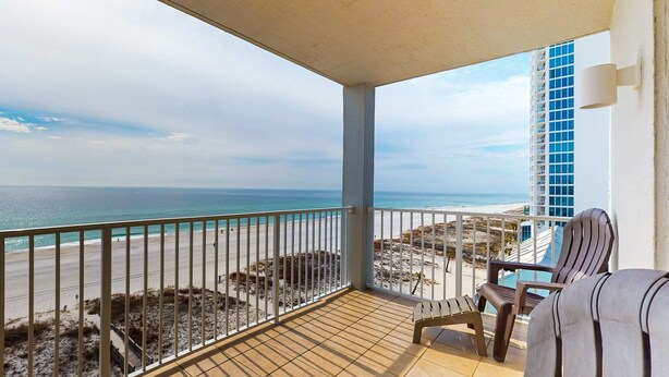Ein Balkon mit Blick auf den Strand und das Meer, ein Stuhl und ein Tisch.