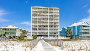 Ein Strandhotel mit mehreren Balkonen, einer Holzpromenade und blauem Himmel.