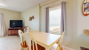 Ein Zimmer mit Esstisch, Stühlen, Fernseher und Blick auf den Strand.