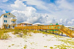 A beachfront property with a wooden boardwalk leading to a building with a balcony. - Beautiful Gulf-front house with private pool, lovely deck, & AC (Gulf Shores)