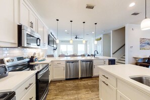 A modern kitchen with stainless steel appliances, white cabinetry, and a central island with a sink. - Beautiful Gulf-front house with private pool, lovely deck, & AC (Gulf Shores)