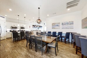 A modern kitchen with white cabinets, stainless steel appliances, and a dining area with wooden tables and chairs. - Beautiful Gulf-front house with private pool, lovely deck, & AC (Gulf Shores)