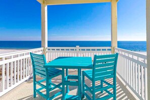 A covered outdoor area with a table and chairs, overlooking a beach and the ocean. - Beautiful Gulf-front house with private pool, lovely deck, & AC (Gulf Shores)