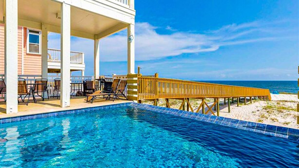 Ein Pool mit Holzterrasse und Liegestühlen, Blick auf den Strand und ein Gebäude mit Balkon.