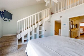 A bedroom with a bed, a staircase with white railings, a TV mounted on the wall, and a bathroom visible through an open door. - Bright and Attractive Home Overlooking the Water w/Free WiFi & Central AC (Gulf Shores)