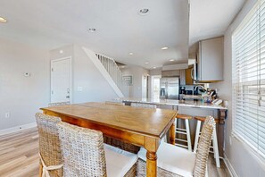 A dining area with a wooden table and wicker chairs, a kitchen with a refrigerator and stove, and a staircase leading to another level. - Bright and Attractive Home Overlooking the Water w/Free WiFi & Central AC (Gulf Shores)