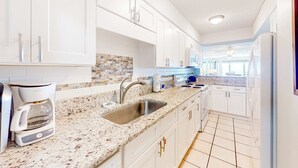 A modern kitchen with white cabinets, a granite countertop, a coffee maker, and a sink. - 8th-floor beachfront condo with Gulf view, waterfront pool, & balcony (Gulf Shores)