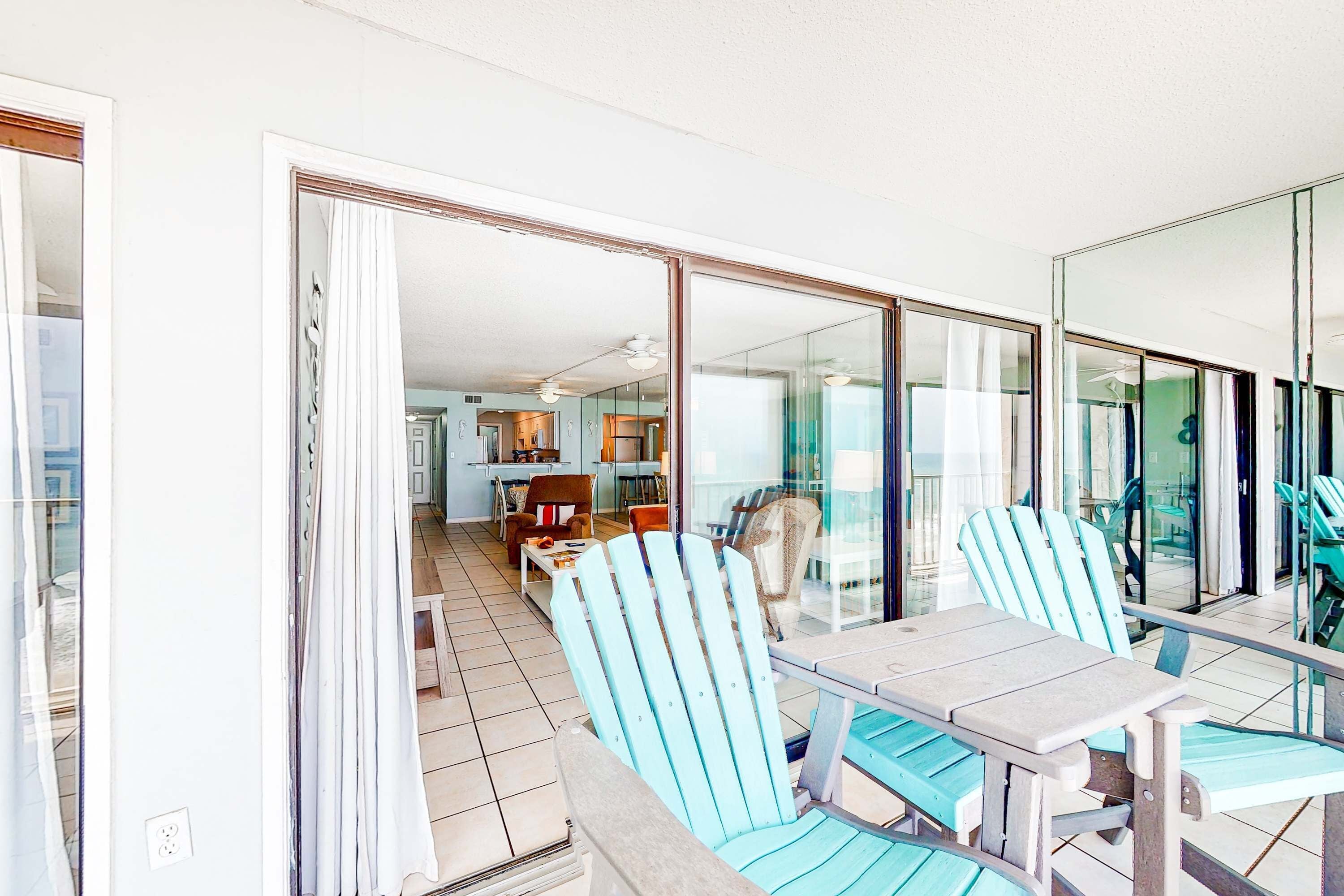 A room with a dining table, chairs, and a view through a glass door to a kitchen and living area.