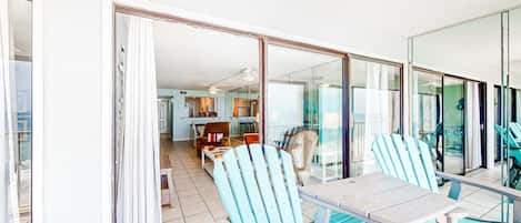 A room with a dining table, chairs, and a view through a glass door to a kitchen and living area.