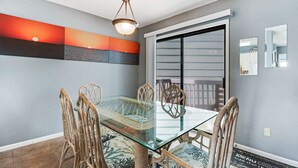 Un coin repas avec une table en verre et des chaises en osier, un luminaire au plafond et une porte-fenêtre coulissante.