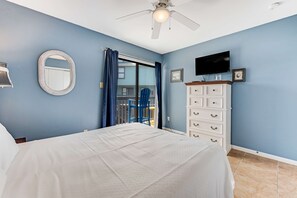 A bedroom with a bed, a ceiling fan, a TV, a dresser, and a window with curtains. - Comfortable Condo at a Beachfront Complex w AC, WiFi, Balconies & Shared Pool (Gulf Shores)