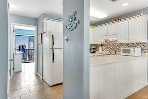 A kitchen with white cabinets, a tiled backsplash, and a refrigerator. - Comfortable Condo at a Beachfront Complex w AC, WiFi, Balconies & Shared Pool (Gulf Shores)