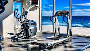 Ett träningsområde med ett löpband och en crosstrainer, en tv och ett stort fönster med utsikt över havet.