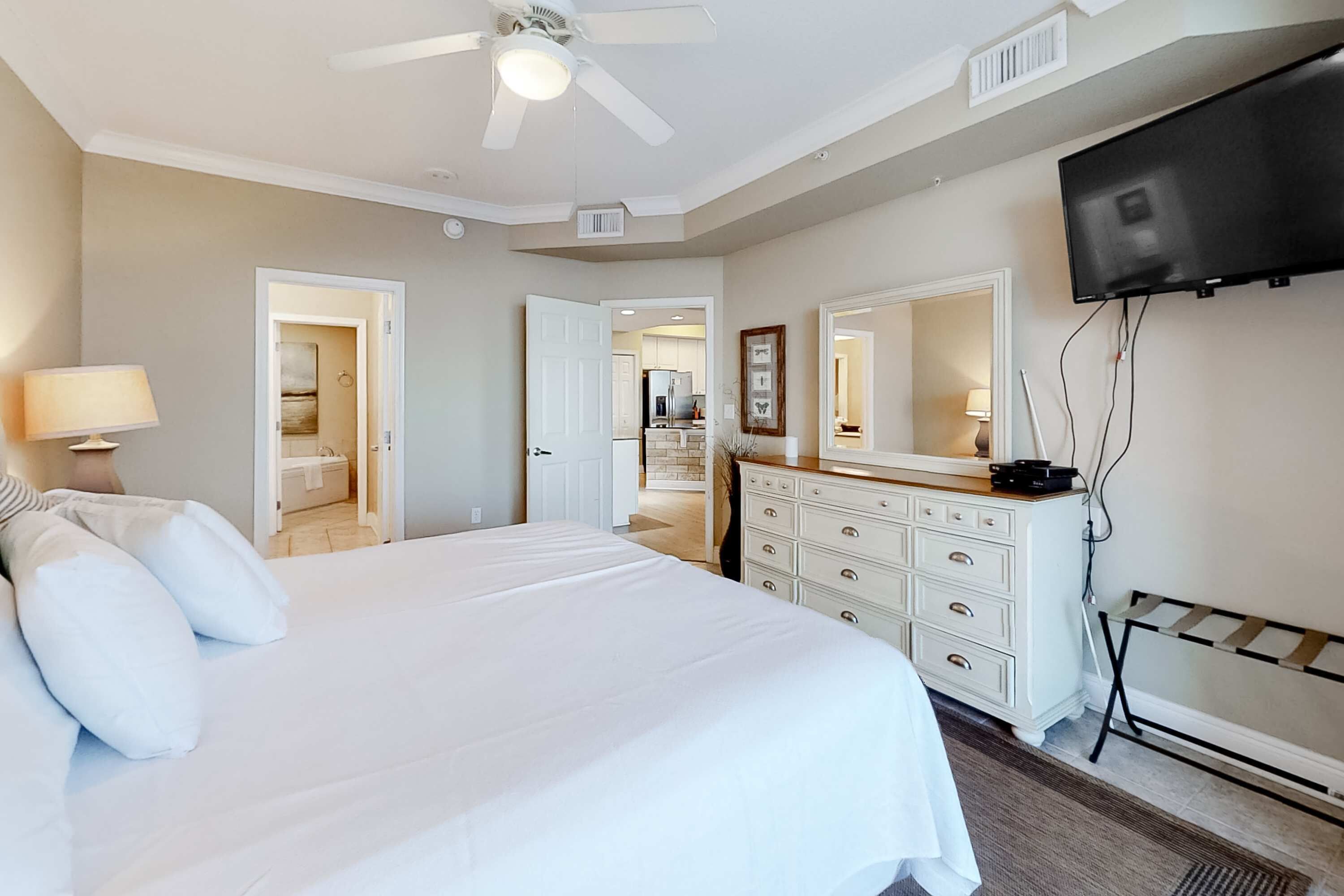 A hotel room with a bed, a dresser, a television, and a ceiling fan.