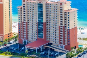 A multi-story hotel with a central atrium, parking lot, and beachfront view. - Lovely Gulf-front condo with pool, sauna, washer dryer, & central AC (Gulf Shores)
