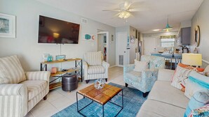 A living room with striped sofas, a coffee table, a TV, and a ceiling fan. - Beachview condo with community pools, grills, and internet (Gulf Shores)