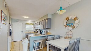 A kitchen with a white countertop, grey cabinets, a white door, and a dining area with a white table and grey chairs. - Beachview condo with community pools, grills, and internet (Gulf Shores)