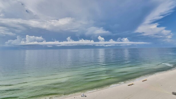 Ein Strand mit klarem Wasser, sandigem Ufer und einem teilweise bewölkten Himmel.