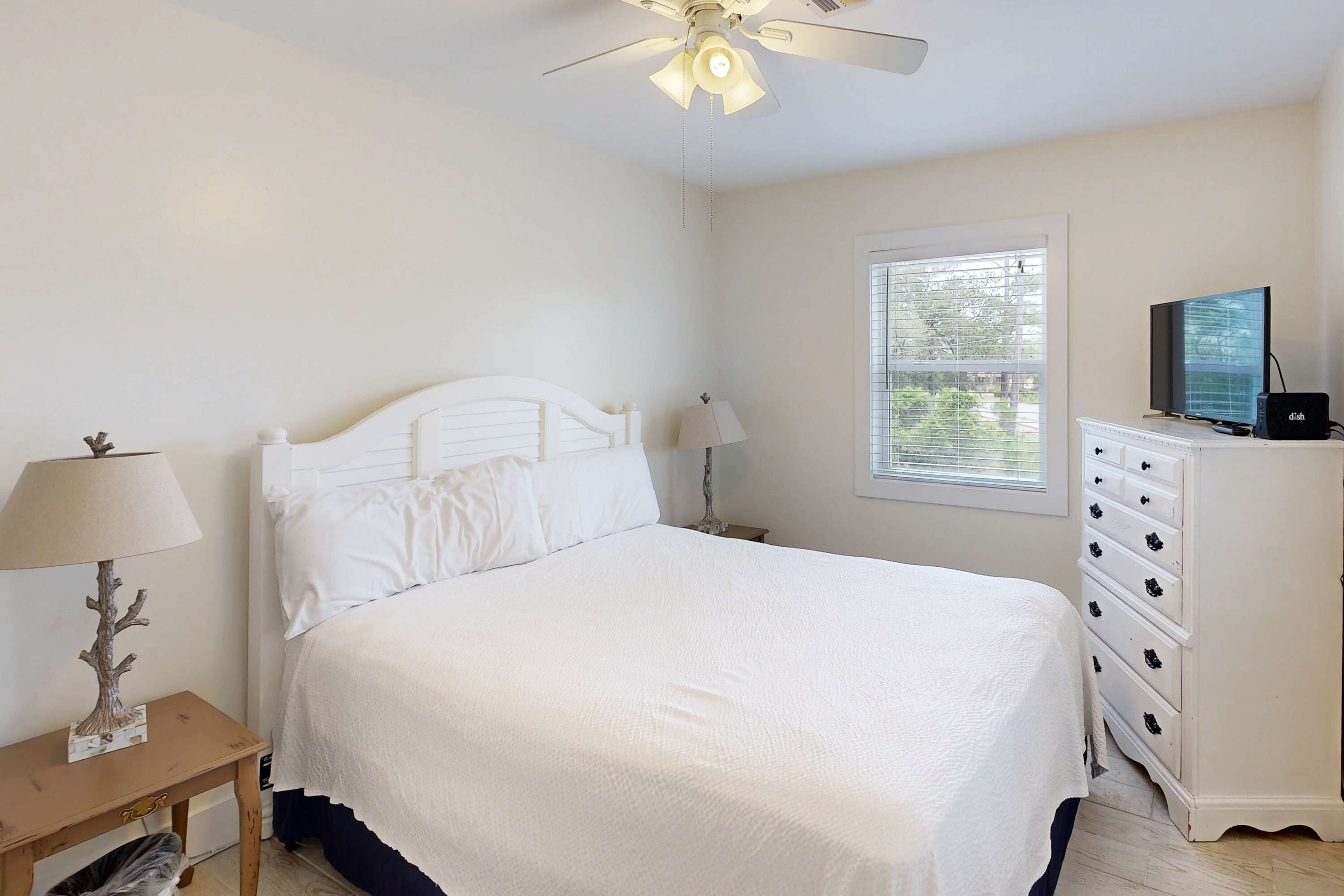Un dormitorio con cama, mesita de noche, cómoda, ventilador de techo y ventana.