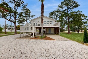 A two-story house with a porch, a small garden, and a gravel driveway. - Dog-friendly bay-view home with central AC - snowbirds welcome (Orange Beach)