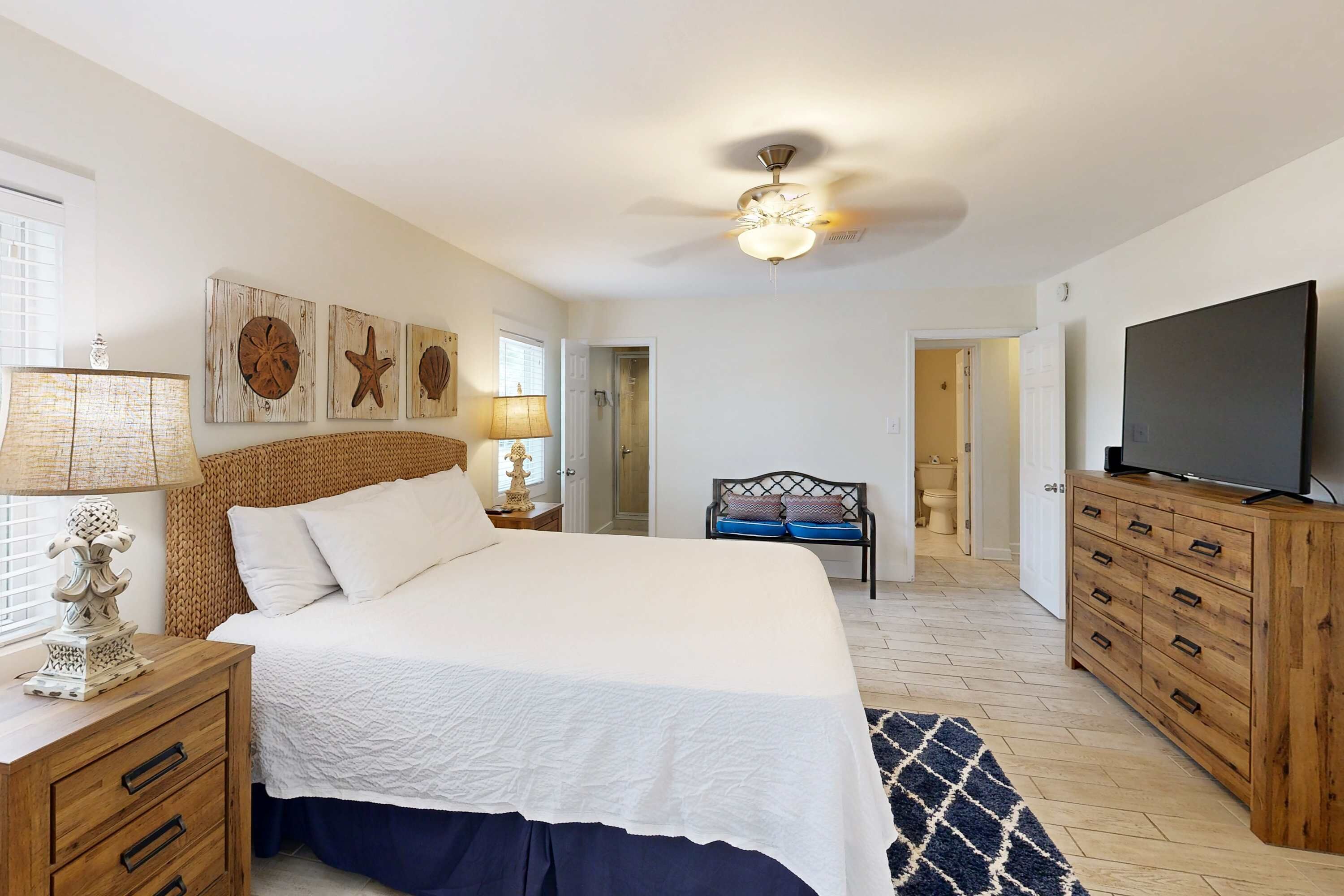 A bedroom with a bed, wooden dresser, TV, and artwork on the wall.