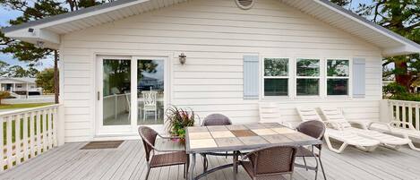 A house with a deck, a dining table with chairs, and a patio area.