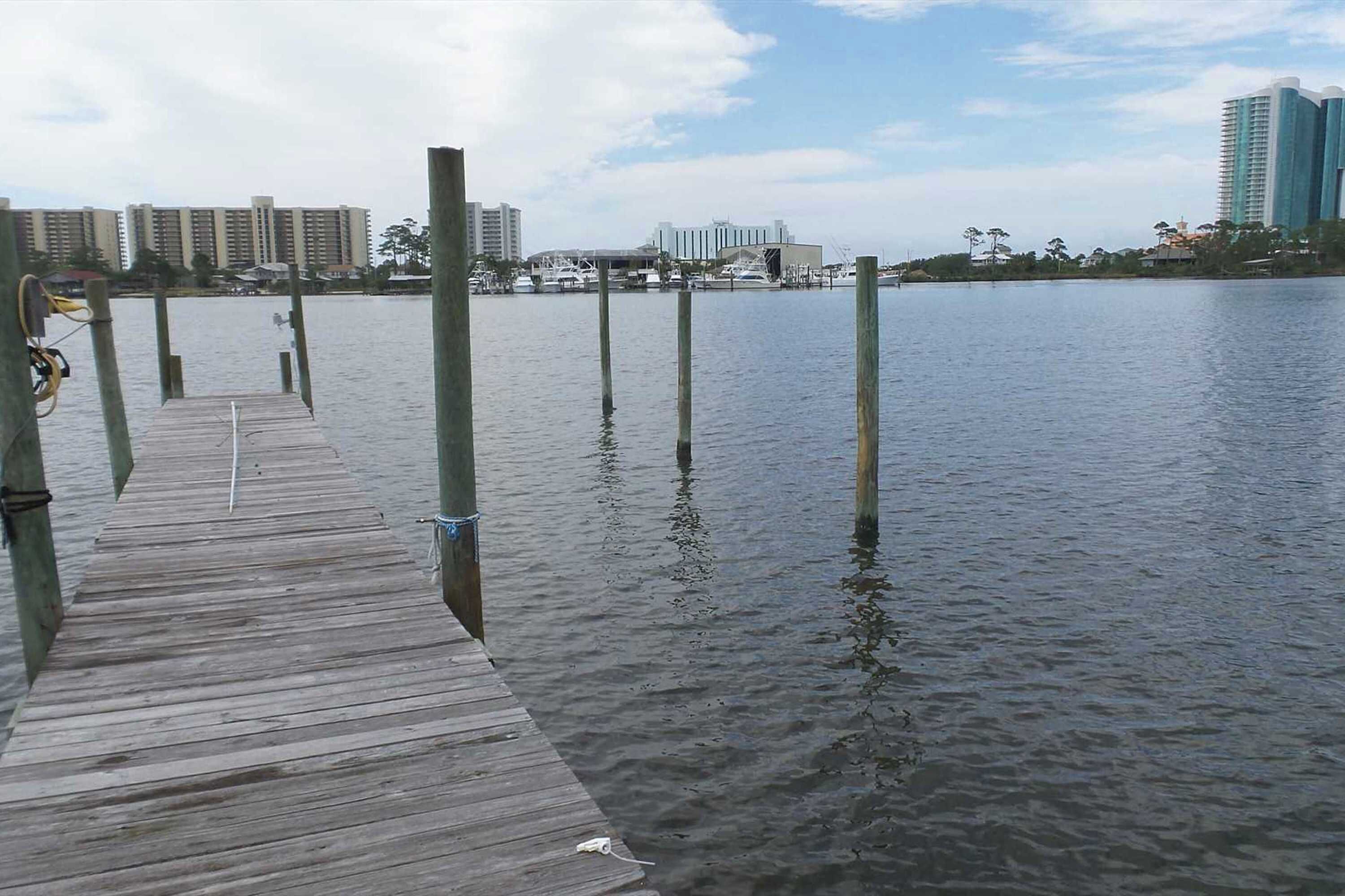 A wooden pier extending into calm water with buildings in the background.