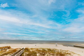 Ein Strand mit einem hölzernen Steg, der zum Ufer führt, feinem Sand und einem klaren Himmel.