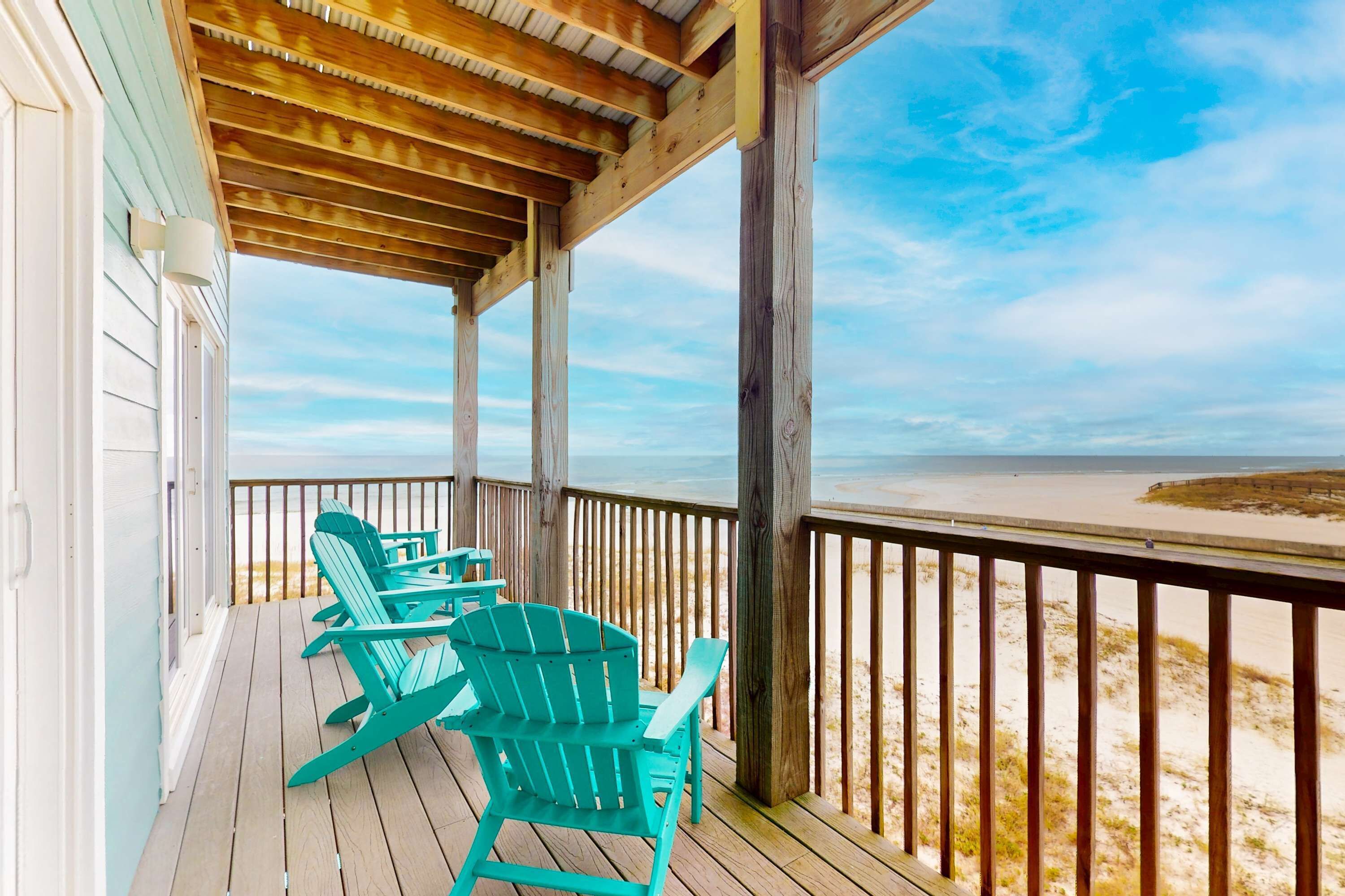 Eine Holzterrasse mit Stühlen mit Blick auf einen Strand.