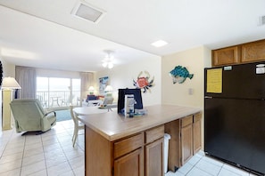 Una cocina con refrigerador, una mesa de comedor, una silla y un ventanal.
