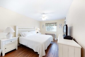Ein Schlafzimmer mit Bett, Nachttischen, Fernseher, einem Fenster mit Vorhängen und einem Deckenventilator.