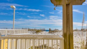 A wooden structure with a metal bell, a white fence, and a sandy beach in the background. - Sunny gulf-front condo with private balcony, shared outdoor pool, great views (Gulf Shores)