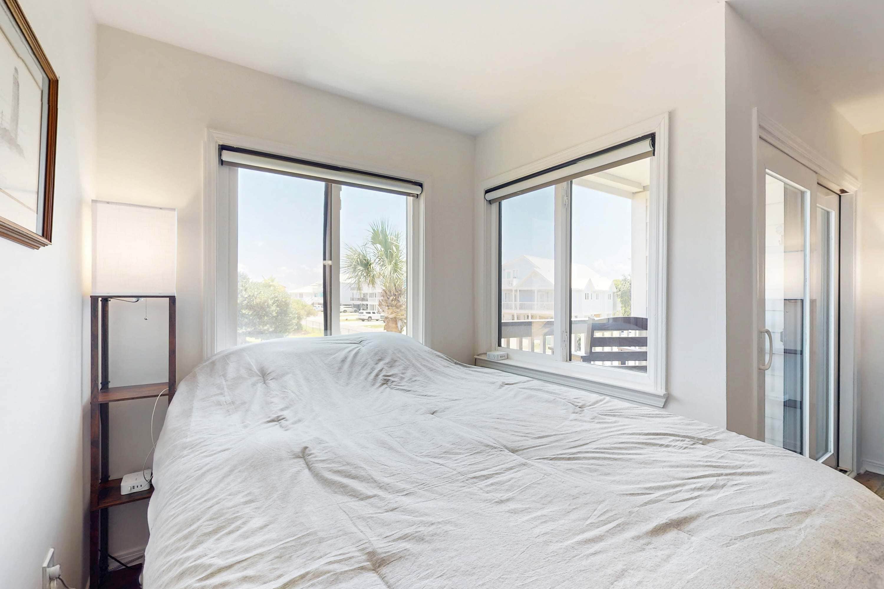 A bedroom with a large bed, two windows, a door, and a small shelf.