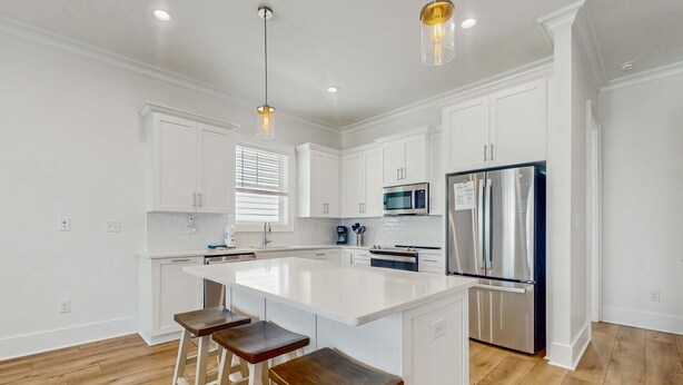 A modern kitchen with white cabinetry, a stainless steel refrigerator, a microwave, and a large island with bar stools. - Brillant cottage near beach with shared pool, balcony, and washer & dryer (Gulf Shores)