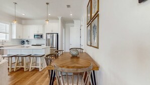 A modern kitchen with white cabinets, a wooden dining table, and bar stools. - Brillant cottage near beach with shared pool, balcony, and washer & dryer (Gulf Shores)