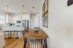 A modern kitchen with white cabinets, a wooden dining table, and bar stools. - Brillant cottage near beach with shared pool, balcony, and washer & dryer (Gulf Shores)