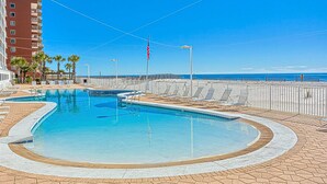 A swimming pool with lounge chairs, a flag, and a view of the ocean.