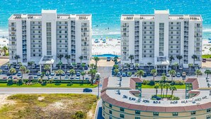 A coastal hotel with multiple high-rise buildings, a parking area, and a beach in the background.