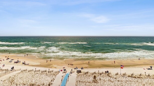 A beach with a pathway leading to the water, a flag, and people on the sand.
