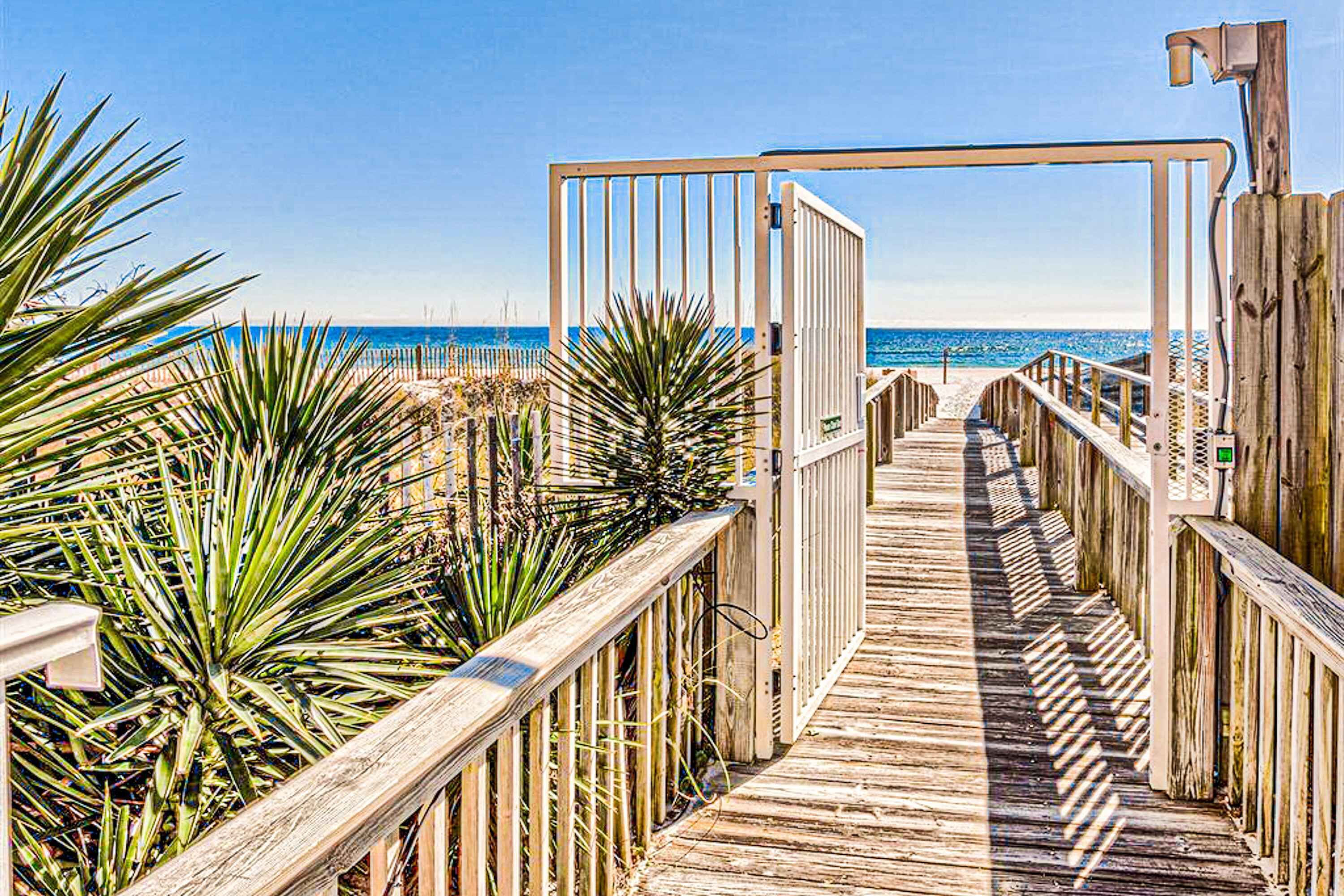A wooden boardwalk leading to a beach, with a gate and railing on one side.