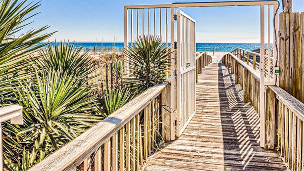 Una passerella in legno che conduce a una spiaggia, con un cancello e una ringhiera su un lato.