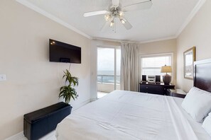 Ein Hotelzimmer mit Bett, Deckenventilator, Fernseher, Pflanze, einem fenster mit Vorhängen, Nachttisch und Lampe.