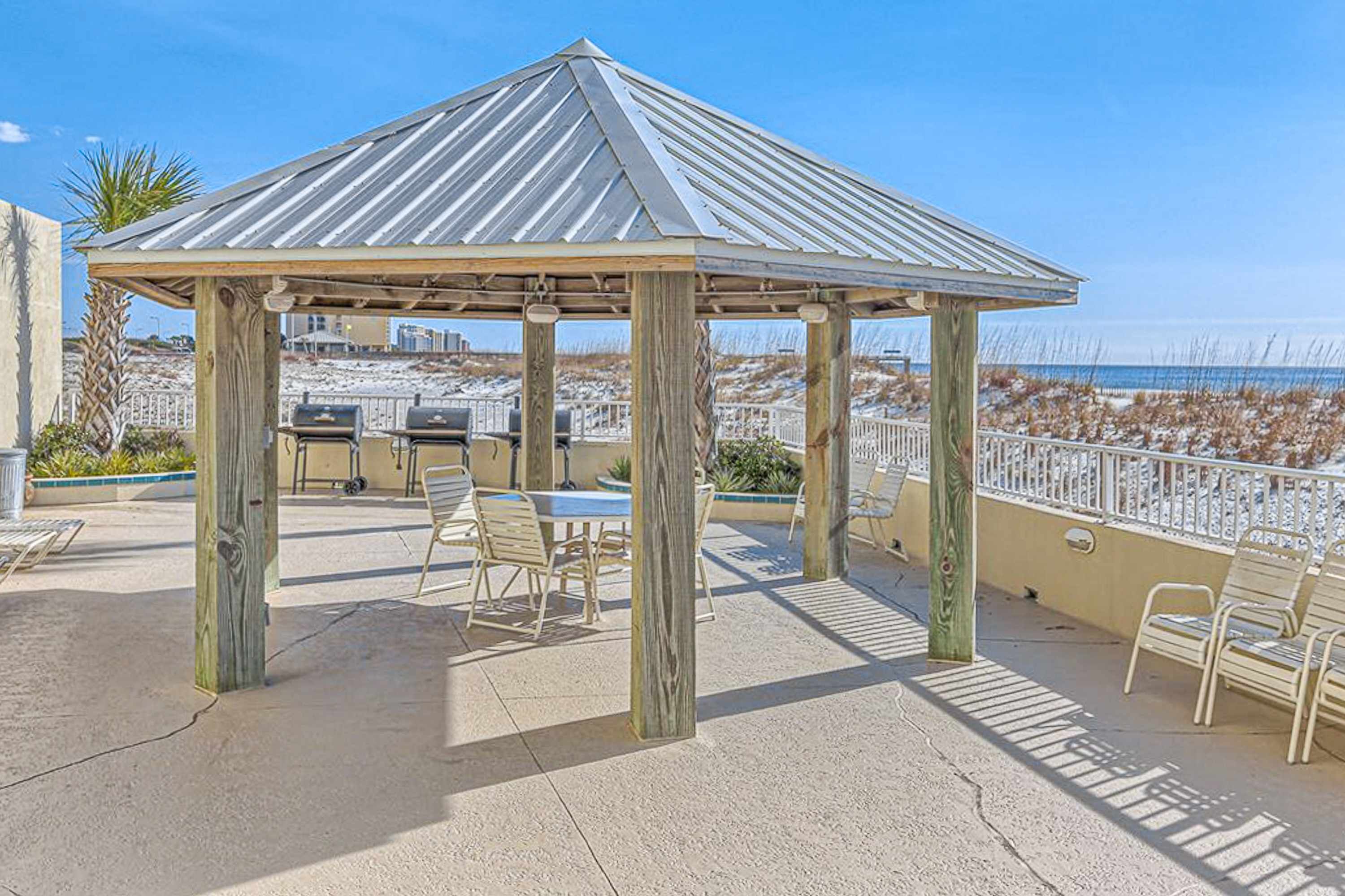 A gazebo with a metal roof, outdoor seating, and a grill.