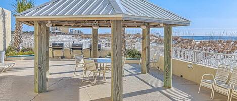 A gazebo with a metal roof, outdoor seating, and a grill.