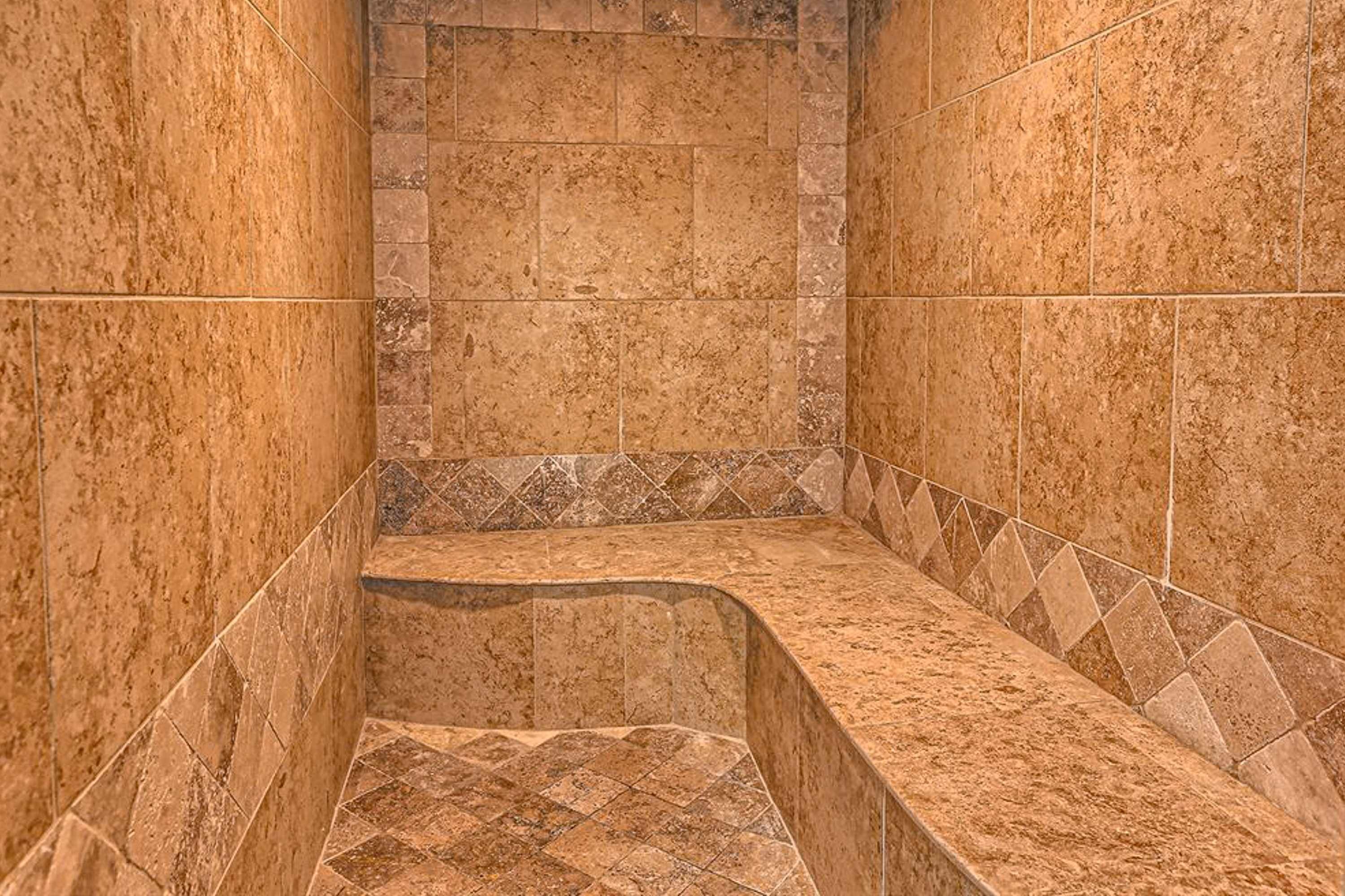 Un baño con piso de mármol, zona de ducha con azulejos y un lavamanos en esquina.
