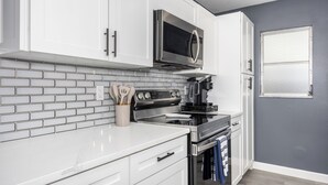 Een moderne keuken met witte kasten, een roestvrijstalen magnetron, een zwart fornuis en een betegelde spatwand.