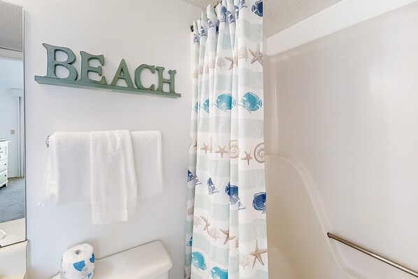 A bathroom with a 'BEACH' sign, a toilet, a towel rack, and a shower curtain with a sea-themed pattern. - Fantastic condo with elevator, WiFi & central AC - beachfront Location (Orange Beach)