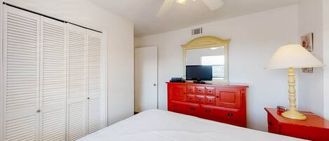 A bedroom with a bed, a red dresser, a television, and a ceiling fan.