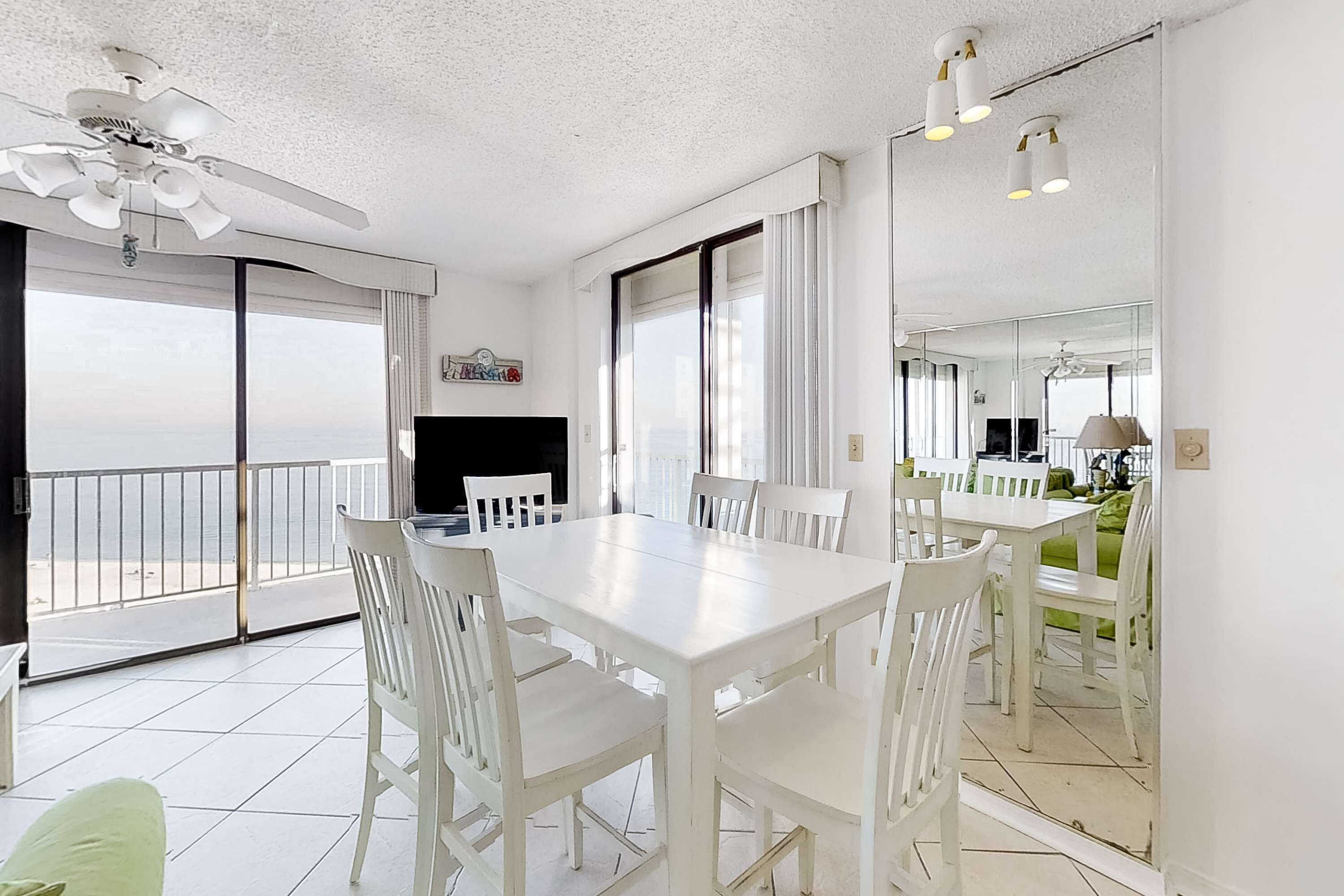 Une pièce spacieuse avec un balcon, des meubles blancs et un ventilateur de plafond.
