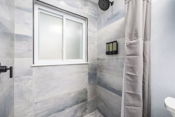 A modern bathroom with a frosted glass window, a shower with a textured curtain, and a wall-mounted soap dispenser. - Backyard Oasis W/ Heated Pool, Bar, Mins to the Beach (Sarasota)